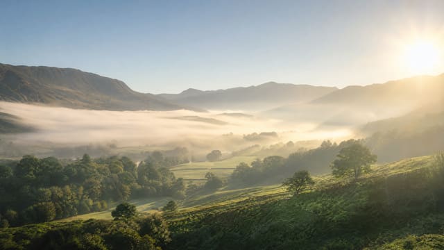 Morning fog lifting over a green valley as the sun breaks through.